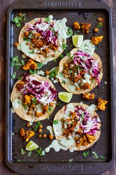 some tacos are sitting on a pan with sauce and garnishes around them