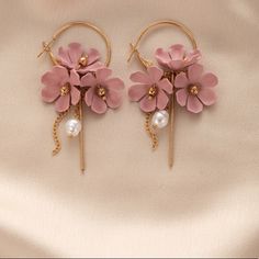 two pink flowers and pearls are attached to gold hoop earrings on a white cloth background