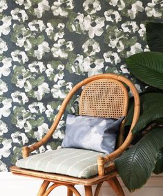 a chair with a pillow on it in front of a flowered wallpaper background