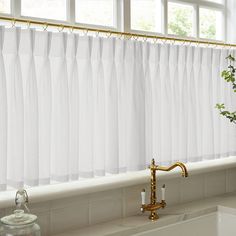 a kitchen window with white curtains and gold faucet