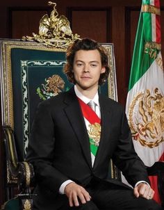 a young man in a suit and tie sitting next to two flags on a table