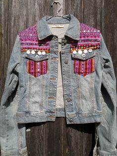 a denim jacket with beaded patches and buttons on the back, hanging against a wooden wall