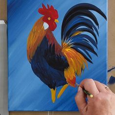 a painting of a rooster is being worked on by someone using acrylic paint