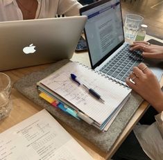 two people sitting at a table with laptops and notebooks in front of them