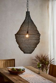 a wooden table topped with a bowl of fruit under a light hanging from the ceiling