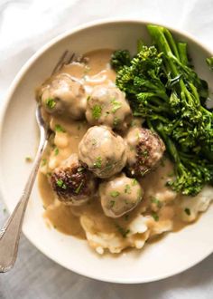 a white plate topped with meatballs and gravy next to broccoli