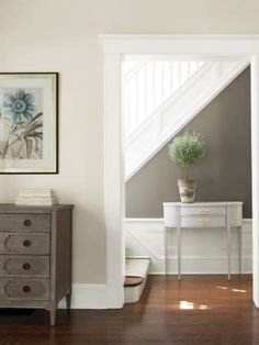 a white dresser sitting next to a wooden floor in a living room under a stair case