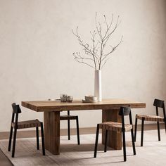 a wooden table with chairs and a vase on top of it next to a white wall