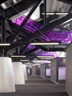 an empty parking garage with purple lighting on the ceiling and concrete pillars in front of it