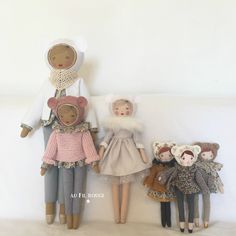 three dolls are standing next to each other on a white surface, one is wearing a dress and the other has a coat