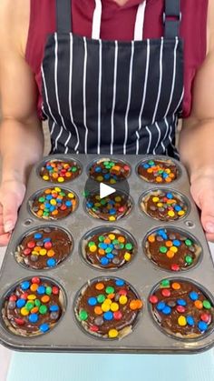 a person holding a muffin pan with cupcakes in it and chocolate frosting