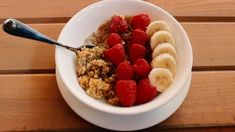 a bowl filled with granola, bananas and raspberries on top of a wooden table