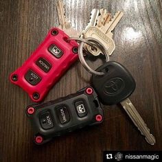 three car keys sitting next to each other on top of a wooden table with red and black keychains