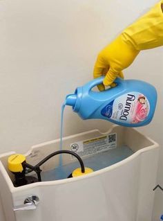 a person in yellow gloves is pouring water into a white toilet with a blue tank