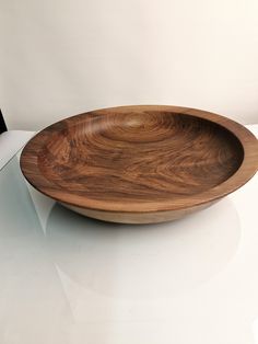 a wooden bowl sitting on top of a white table next to a black object in the background