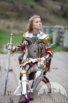 a woman dressed as a knight sitting on a wooden platform with two swords in her hand