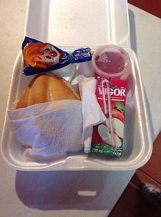 a plastic container filled with food on top of a white table next to a cup