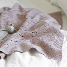 a teddy bear laying on top of a bed next to a pink knitted blanket