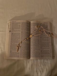 an open bible with rosary beads and cross on it laying on top of a bed