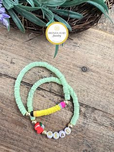 two bracelets with beads and charms on top of a wooden table next to flowers