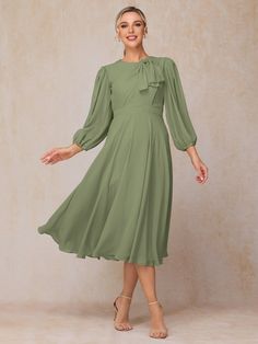 a woman wearing a green dress with long sleeves and a bow at the neckline