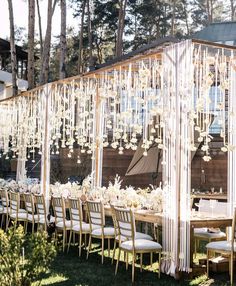 a long table with white flowers on it in front of a wooden structure that is surrounded by greenery