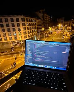 an open laptop computer sitting on top of a wooden desk next to a window at night