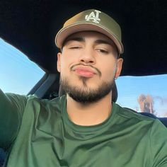 a man with a beard wearing a baseball cap and green shirt in the back seat of a car