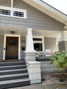 a gray house with white trim and steps leading up to the front door that leads into the porch