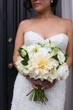 a woman in a wedding dress holding a bouquet of white and yellow flowers with greenery