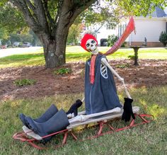 a skeleton sitting on top of a sled in the grass next to a tree