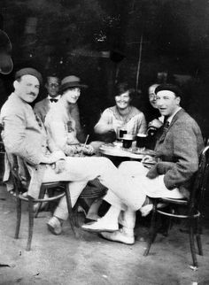 an old black and white photo of people sitting around a table with drinks in front of them