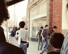 a group of people standing on the side of a road next to a brick building