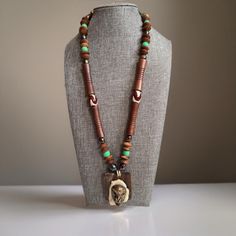 Beautiful and unique. One of a kind statement necklace. Leather cord. Wooden beads of varying sizes. Seed beads. Trade beads. Glass beads. The pendant is a brass tribal mask design attached to a slab of stone/geode which is attached to a piece of wood. Native ethnic mask ceremony. Please see pictures for details and measurements. 72475 Bronze Bohemian Beaded Necklace With Wooden Beads, Bohemian Bronze Beaded Necklace With Wooden Beads, Bohemian Bronze Necklace With Wooden Beads, Beaded Leather Necklace, Necklace Leather Cord, Leather Beaded Necklace, Necklace Leather, Trade Beads, Bead Leather