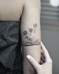 a woman with a book and flowers tattoo on her arm