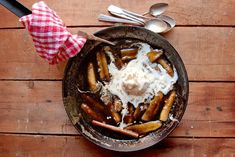 a pan filled with french fries covered in sour cream next to spoons and a checkered napkin