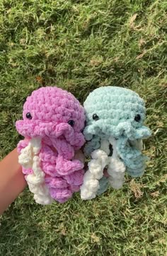 two crocheted stuffed animals sitting next to each other on the grass in front of someone's hand