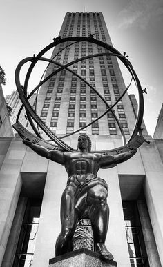 a statue in front of a tall building with a man holding a ring around his neck