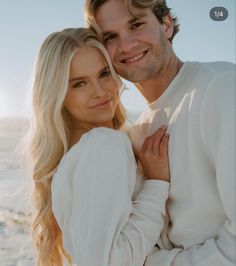 a man and woman standing next to each other in front of the ocean with their arms around each other