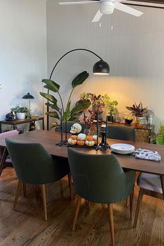 a dining room table with green chairs and plates on it, surrounded by potted plants