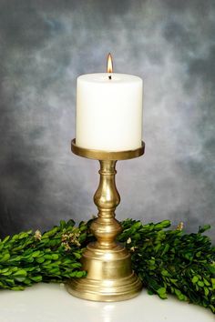 a white candle sitting on top of a table next to green leaves and greenery