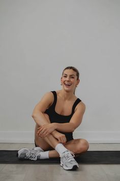 a woman sitting on the floor with her arms crossed and legs crossed, smiling at the camera