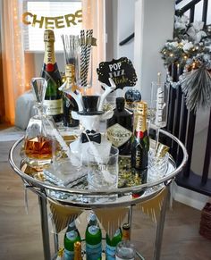 a bar cart filled with liquor bottles and champagne glasses on top of a wooden floor next to a christmas tree