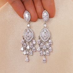 a pair of diamond earrings being held by someone's hand