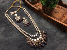 Amethyst and Kundan Long Layered Necklace Set For Women & Girls Material : Kundan, natural stone, faux pearl, glass, thread, and metal Dimension : Necklace - 28 x 2.5 inches approx. Earrings - 2.5 x 1 inches approx. Be the showstopper this wedding season with our Stone Kundan Long Layered Necklace Set. It has two layers of pearls and kundan stones. The second layer is given a royal look with grey colored glass beads and natural stones that dangle elegantly from kundan stones. Kundan stones, pear Elegant Purple Kundan Necklace As Gift, Elegant Purple Kundan Necklace For Wedding, Elegant Purple Kundan Necklace For Festive Occasions, Elegant Purple Jewelry Set For Festive Occasion, Festive Purple Necklace For Wedding, Long Kundan Necklace, Pakistani Necklace, Lavender Jewelry, Jewelry Indian Wedding