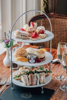 three tiered trays filled with sandwiches and pastries on top of a wooden table