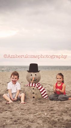 two children sitting in front of a snowman on the beach