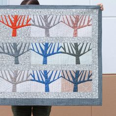 a woman is holding up a quilt with trees on the front and back, in different colors