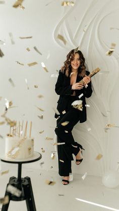 a woman standing in front of a cake with gold confetti falling from it