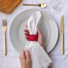 a person holding a napkin on top of a white plate next to silverware and utensils